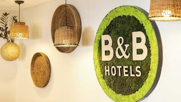 A circular sign with 'B&B HOTELS' text, surrounded by woven wall hangings and pendant lights.