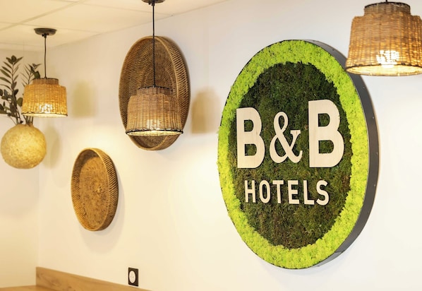 Un letrero circular con el texto 'B&B HOTELS', rodeado de tapices y luces colgantes.