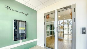 A reception area with a green wall, a glass door leading outside, and a self-service kiosk. - B&B Hotel La Réunion Aéroport (Sainte Marie)
