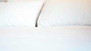 Een bed met witte lakens en kussens.