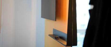 A modern room with a flat-screen TV mounted on a wall, a small shelf below it, and a door with a black frame.