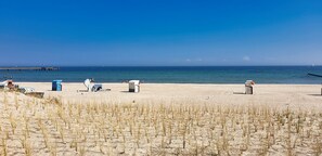 A beach with a few beach chairs, a trash bin, and a lifeguard stand. - Stylish vacation apartment Seeluft in Großenbrode. Balcony with wonderful sea view. Family-friendly furnishings and maximum sleeping comfort in a box-spring bed. Practical washing machine and iron (Großenbrode)