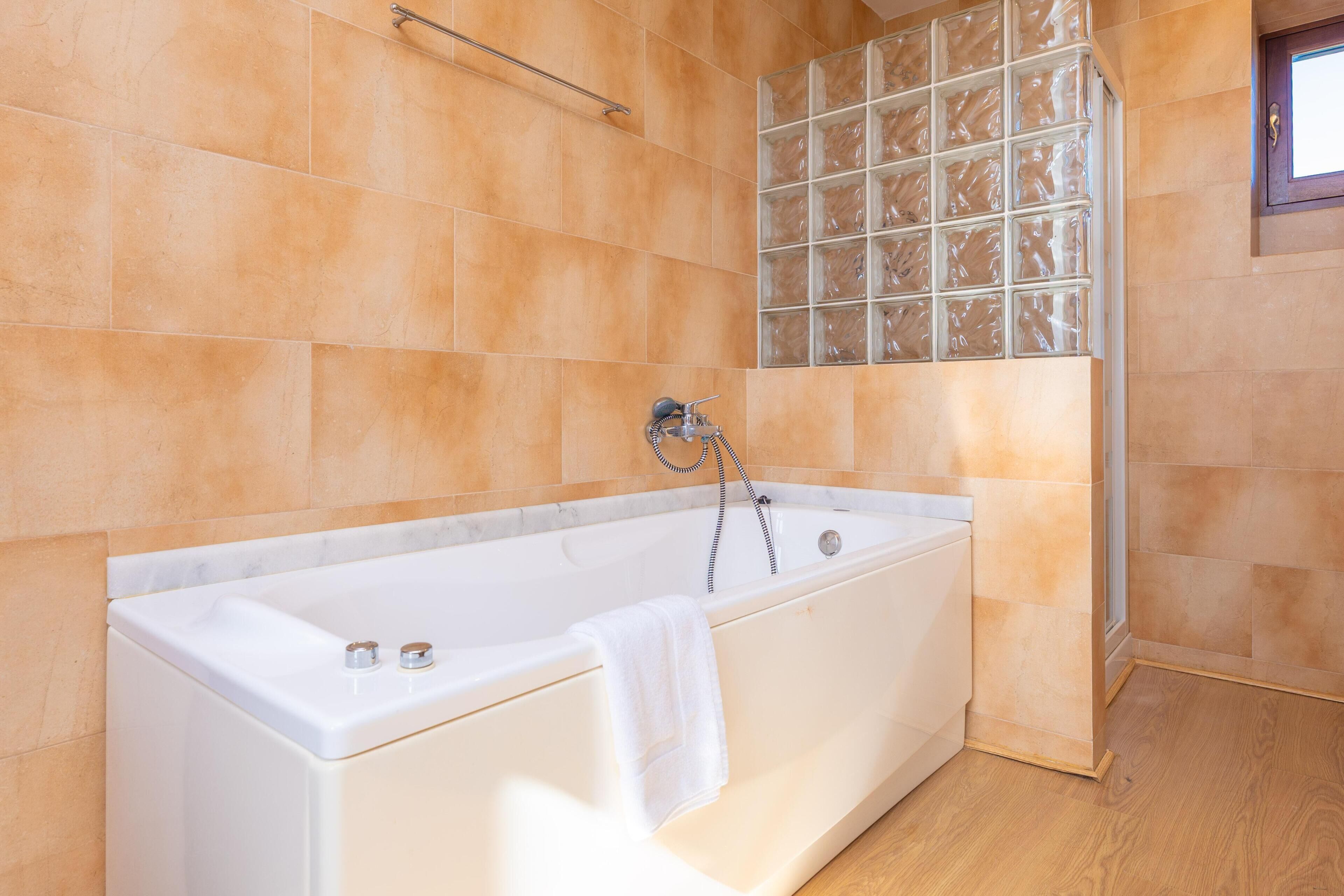 A modern bathroom with a large bathtub, a glass block wall, and a wooden floor.