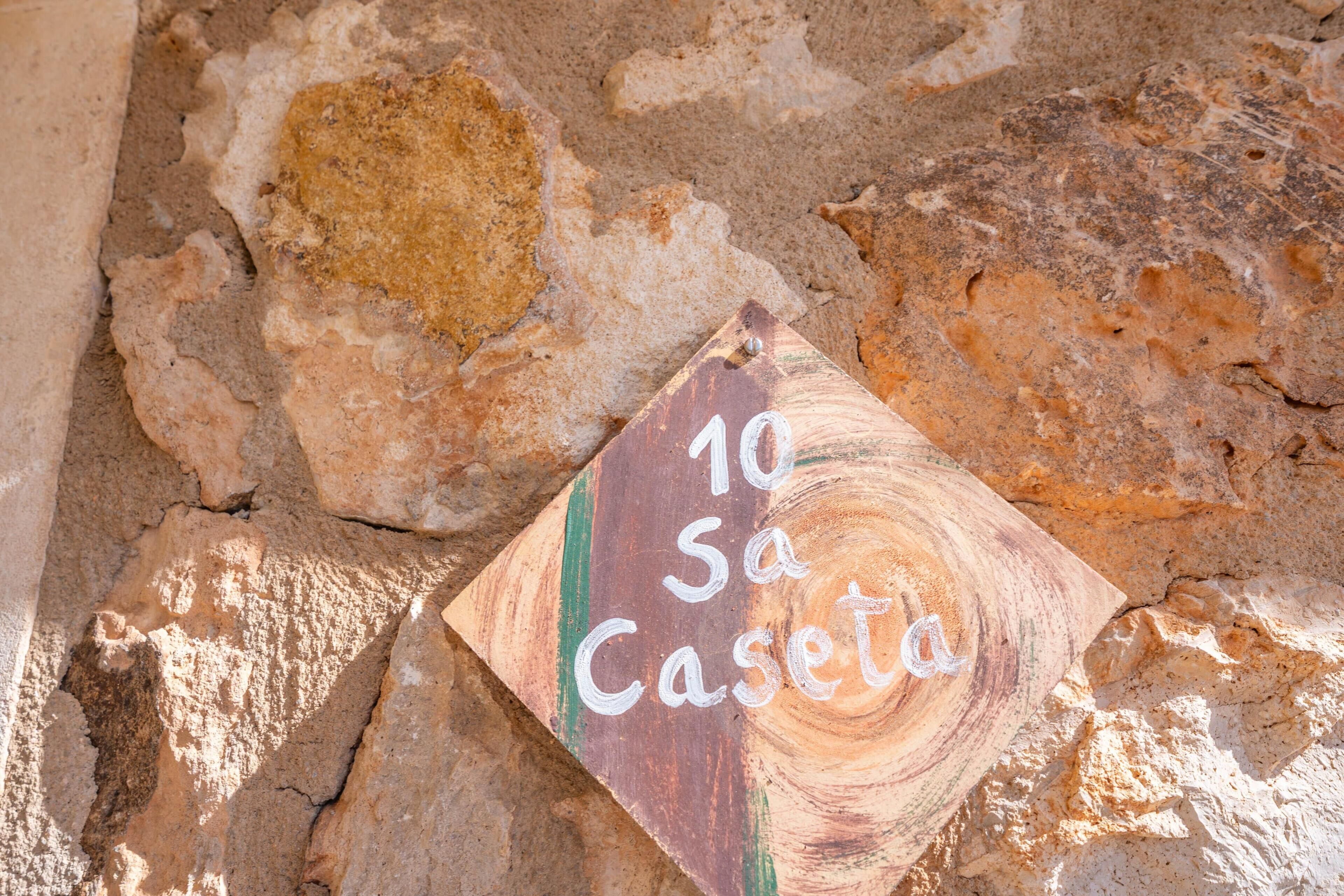 A stone wall with a wooden sign that reads "10 Sa Caseta."