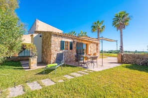 Una casa de piedra con un patio, mobiliario exterior y palmeras.