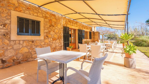 Eine Außenpatio-Terrasse mit Steinmauern, weißen Korbmöbeln und einem Baldachin.
