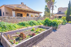 Un muro de piedra, un jardín con bancales y una casa con techo de tejas.