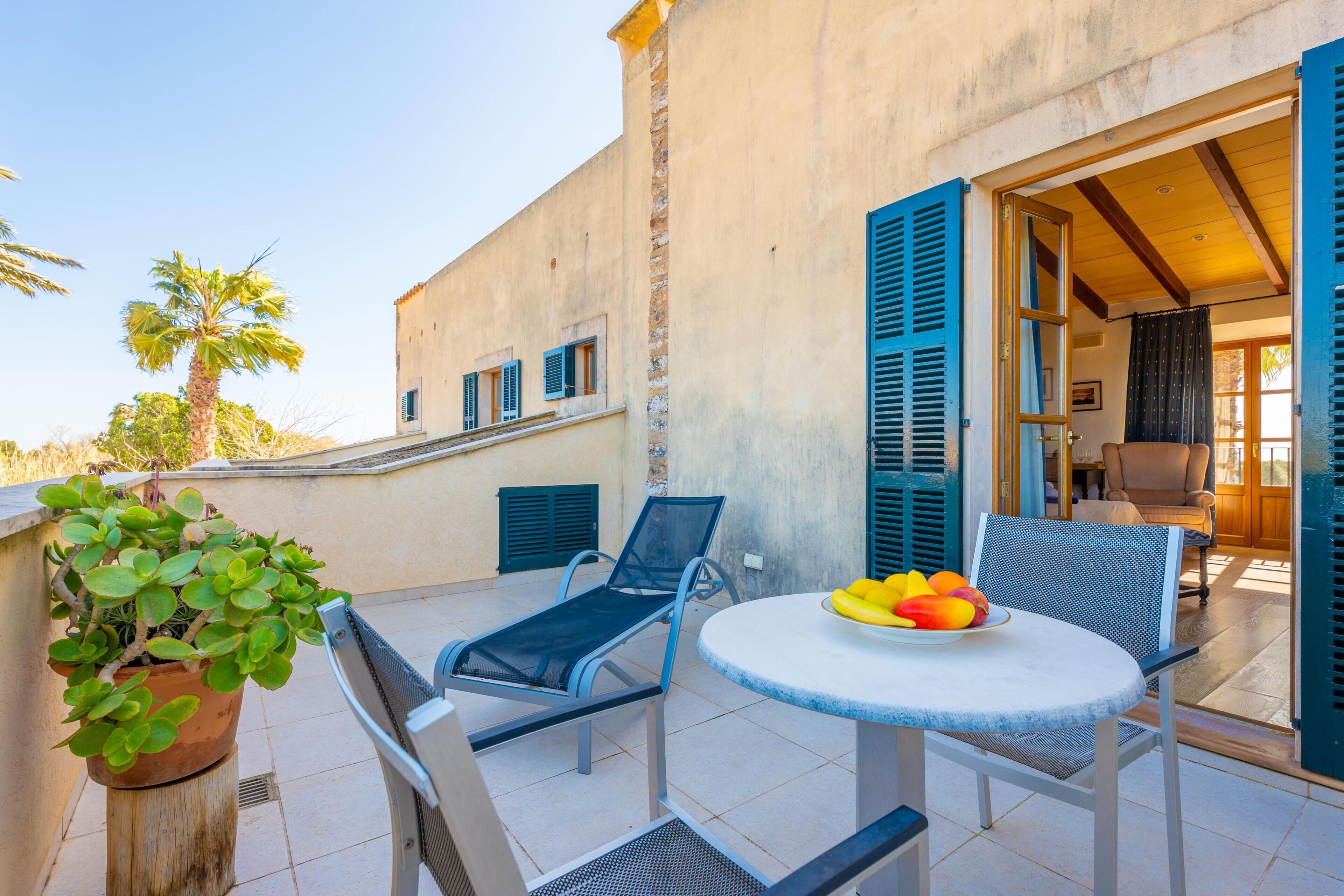 A terrace with two lounge chairs, a round table with fruit, and a potted plant.