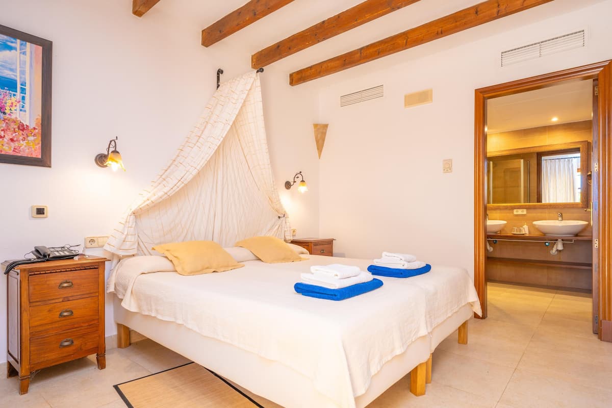 Un dormitorio con cama, mesitas de noche, un espejo y un baño visible a través de una puerta abierta.