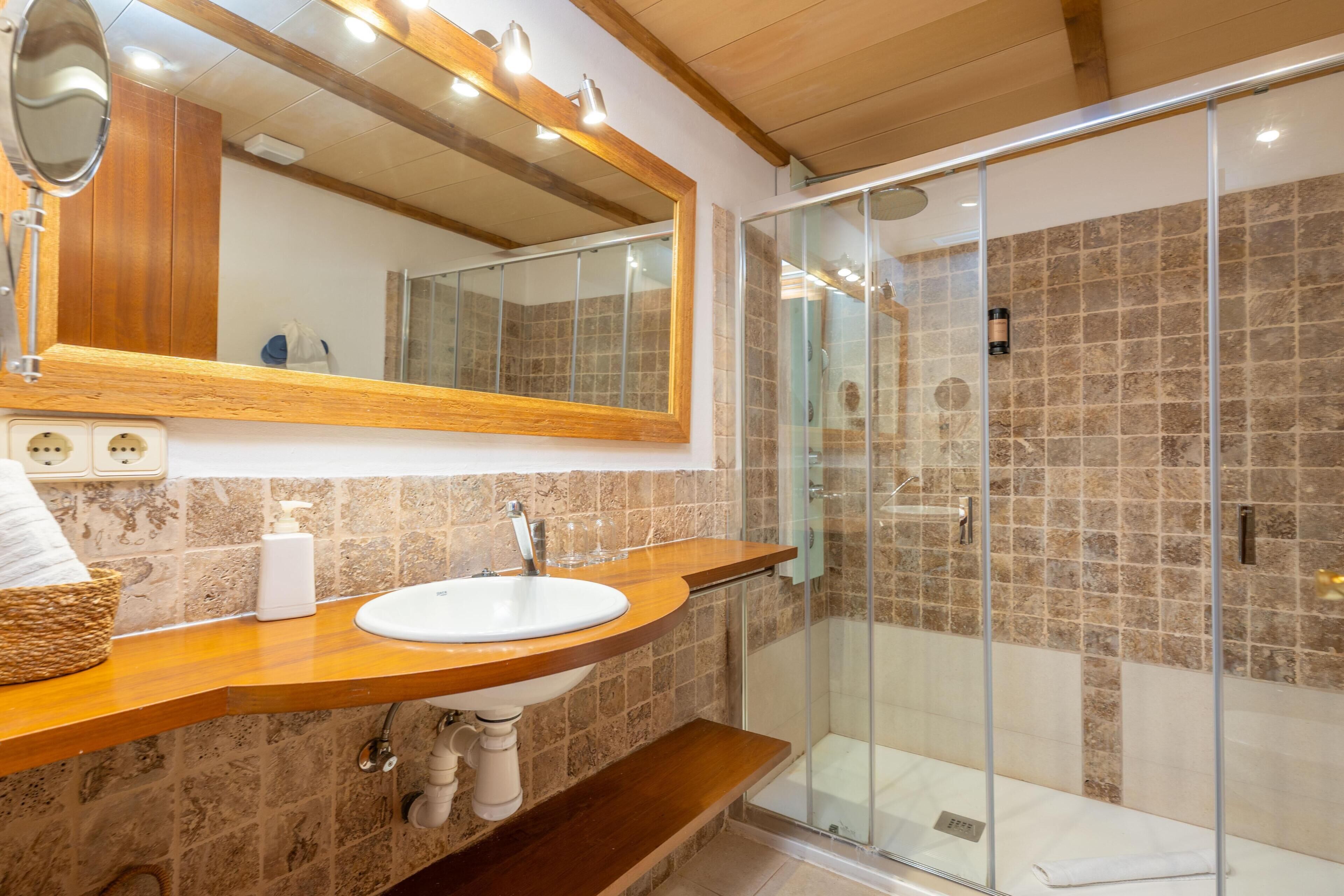 A bathroom with a wooden vanity, a white sink, a large mirror, and a glass-enclosed shower.