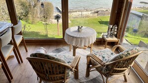Une pièce avec vue sur la mer, des meubles en osier, une table ronde recouverte d’une nappe blanche et une petite table d’appoint décorative.