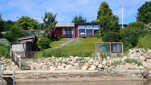 Une propriété au bord du lac, dotée d’une jetée en bois, d’un bâtiment rouge aux grandes fenêtres et d’un chemin de pierre menant à l’eau.
