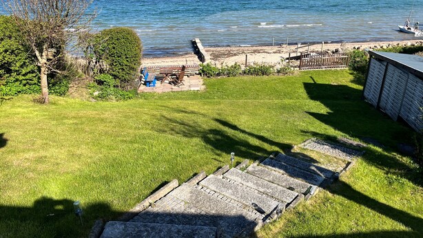 Une zone herbeuse avec un sentier en pierre menant à une plage, une clôture en bois et un bateau sur l’eau.