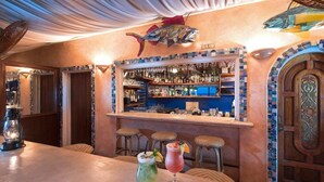 Zona de bar con mostrador, taburetes y una variedad de botellas y vasos.