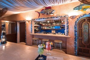A bar area with a counter, stools, and a variety of bottles and glasses. - Little Arches Boutique Hotel Barbados (Oistins)