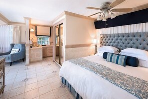 Habitación de hotel con cama, silla, escritorio, televisor y ventilador de techo.