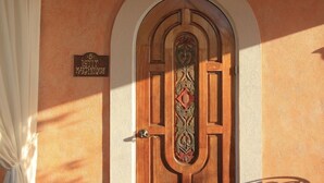 Una puerta de madera con un diseño ornamentado, una señal encima y una cortina blanca a la izquierda.