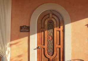A wooden door with an ornate design, a sign above it, and a white curtain to the left. - Little Arches Boutique Hotel Barbados (Oistins)
