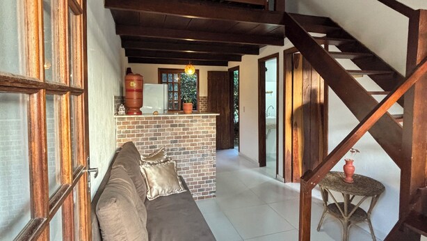 A spacious living area with a high ceiling, a wooden staircase, and a cozy seating area with a sofa and cushions. - Pousada Jardim da Vida (Caeté-Açu)