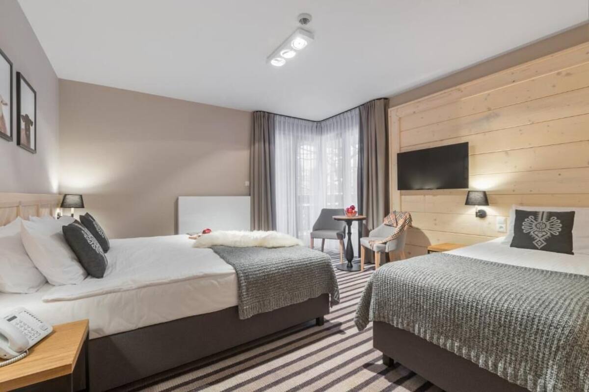 Ein Hotelzimmer mit zwei Betten, einem Fernseher, einem Telefon, einem Sessel und einem kleinen Tisch.
