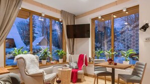 Un interno moderno con un divano, sedie, un tavolo da pranzo e ampie finestre vista alberi e una casa.