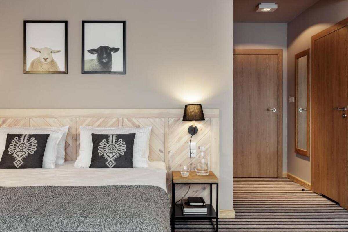 Ein Schlafzimmer mit einem Bett, zwei gerahmten Bildern, einer Nachttischlampe, einem Nachttisch und einer Tür.