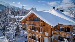 Un chalet in legno a più piani con balconi, immerso in un paesaggio innevato di alberi e montagne.