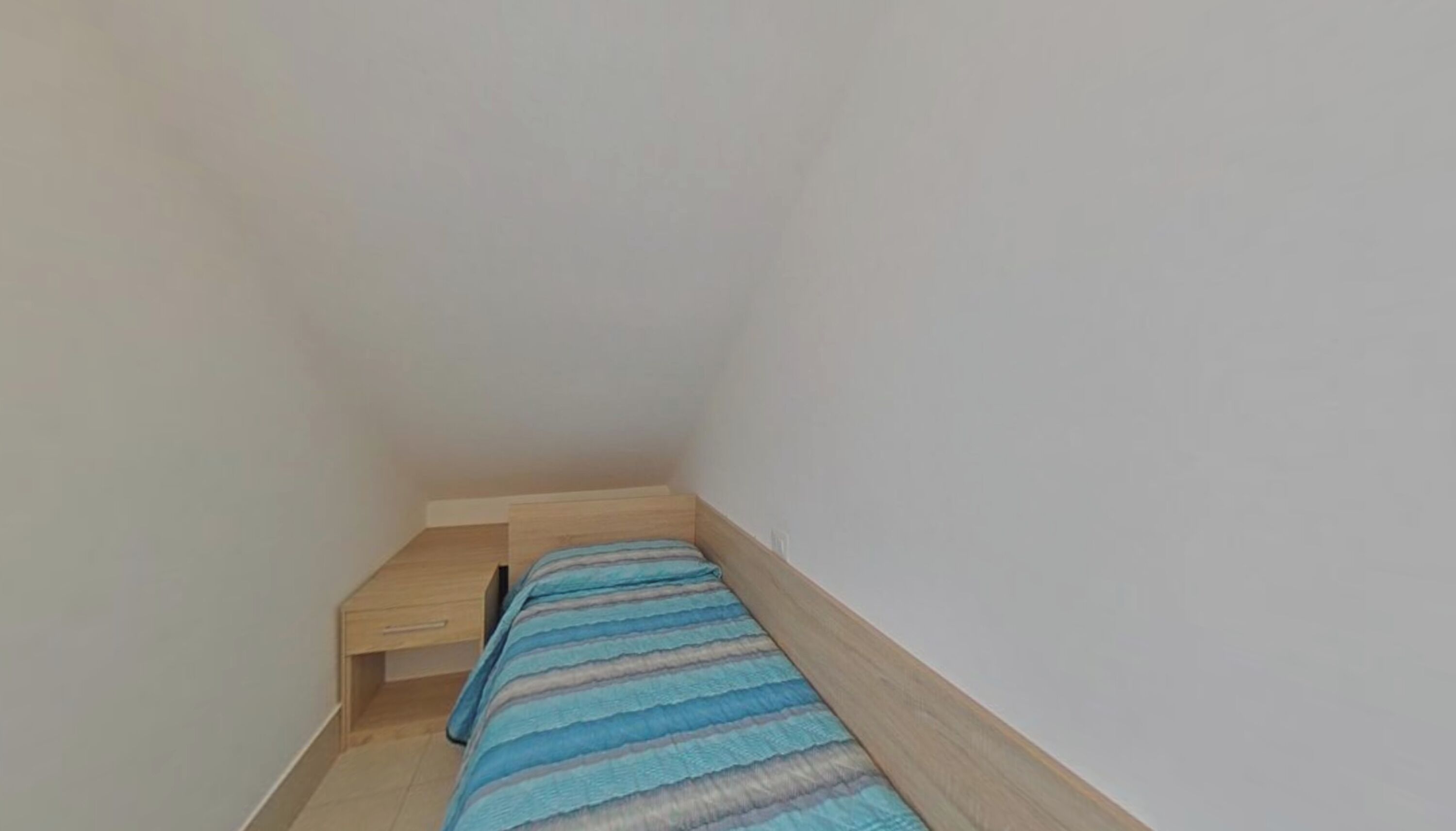 Una habitación pequeña con una cama individual, cabecera de madera y mesita de noche.