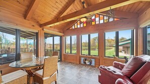 A wooden interior with a glass table, wicker chairs, a leather sofa, and large windows offering a view of the outdoors. - Experience the quiet beauty of the Amish countryside at Sprinkle Bottom Lodge. (Sullivan)