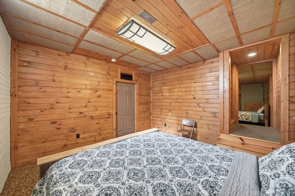 A wooden-paneled room with a bed, a chair, a door, and a mirror.