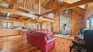 A spacious log cabin interior with a red leather sofa, wooden floors, a stone fireplace, and a high ceiling with exposed beams. - Experience the quiet beauty of the Amish countryside at Sprinkle Bottom Lodge. (Sullivan)