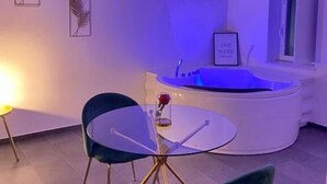 Ein modernes Zimmer mit einem Glastisch, zwei Stühlen, einer Badewanne und gerahmten Kunstwerken an der Wand.