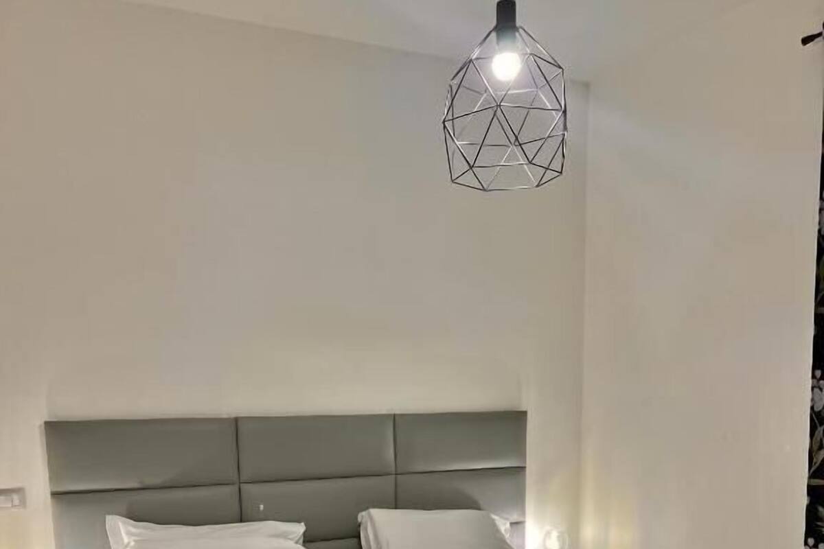 A hotel room with two beds, a geometric pendant light, and patterned floor tiles.