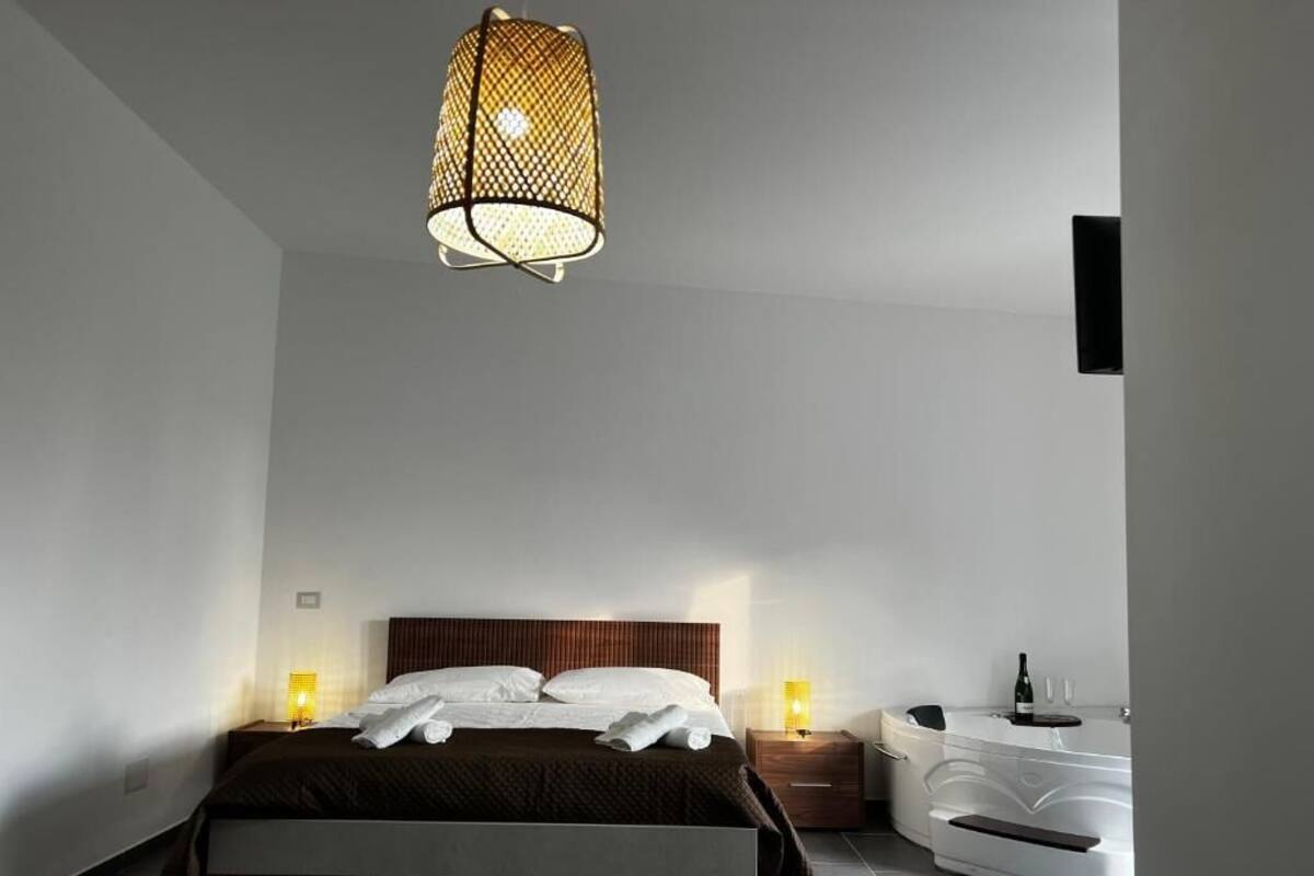 A modern bedroom with a bed, bedside lamps, a nightstand, a white dresser, and a hanging light fixture.