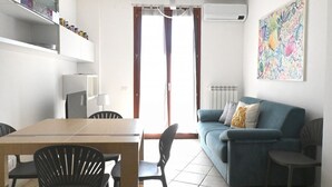 A modern living room with a dining table, chairs, a sofa, and a colorful abstract painting on the wall.