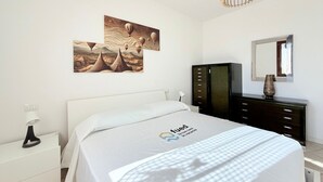 A bedroom with a bed, a nightstand, a dresser, a mirror, and wall art.
