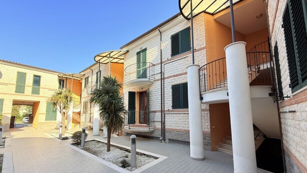 A courtyard with a building featuring a balcony, a staircase, and a pathway.