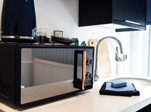 Una cocina con microondas, un lavabo y una tabla de cortar.