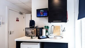 Eine kompakte Küche mit Mikrowelle, Toaster, Spüle und einem Fernseher, der über der Arbeitsfläche angebracht ist.