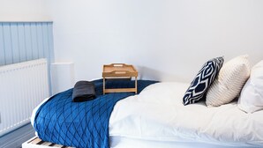 Ein ordentlich gemachtes Bett mit einer blauen Steudecke, weißen Kissen und einem Holztablett.