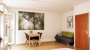 A room with a dining table, chairs, a sofa, a large forest-themed painting, and a wooden door. - Vacation apartment Schwarzwaldnest 1 - central, accessible and quiet (Emmendingen)