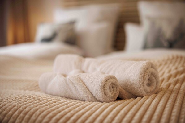 A neatly made bed with rolled white towels and a textured beige bedspread.