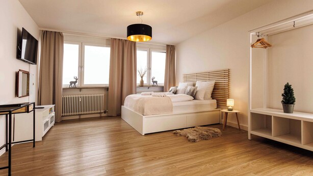 A bedroom with a bed, bedside table, lamp, radiator, and a TV on the wall. - Vacation apartment Schwarzwaldnest 1 - central, accessible and quiet (Emmendingen)