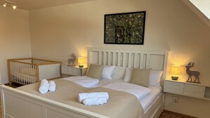 Een slaapkamer met een groot bed, een wiegje, bedlampjes en een lijst met een afbeelding aan de muur.