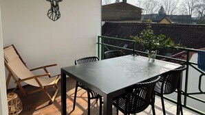 Een balkon met een tafel en stoelen, een decoratief kunstwerk en uitzicht op gebouwen en bomen.