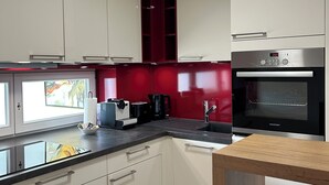 Een moderne keuken met witte kastjes, een rode achterwand, een ingebouwde oven en een raam met uitzicht.
