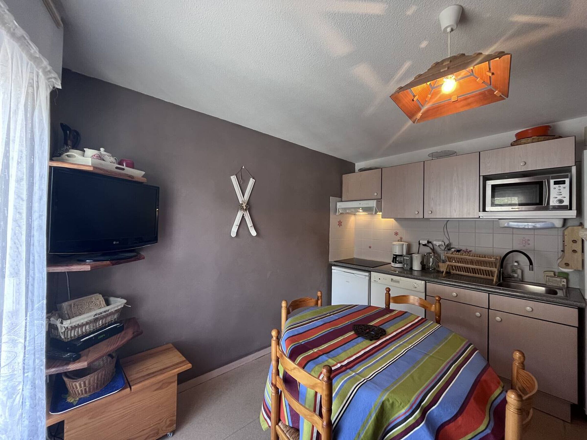 A compact room with a bed, a TV, a microwave, and a kitchenette.