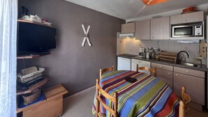 Quarto compacto com cama, televisão, micro-ondas e pequeno espaço de cozinha.