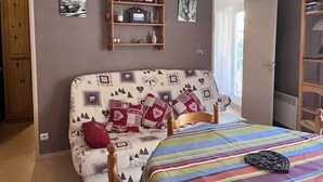 Quarto com cama, cabeceira de madeira, prateleira com quadros e porta para outro cômodo.
