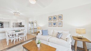 A modern living room with a white sofa, a coffee table, and a dining area with a white table and chairs.